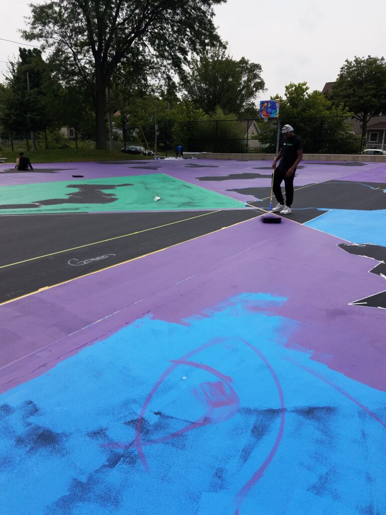 A man is painting the floor of a basketball court.