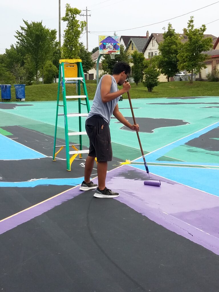 A man is painting the floor of a basketball court.